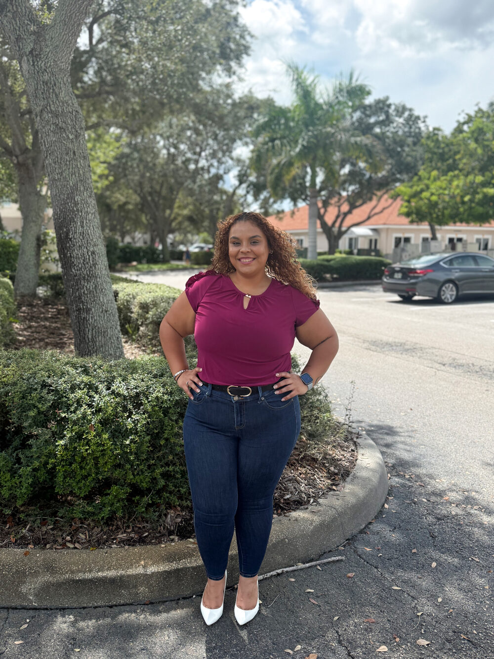 Bryanna standing outdoors in a magenta blouse and dark jeans, smiling at the camera