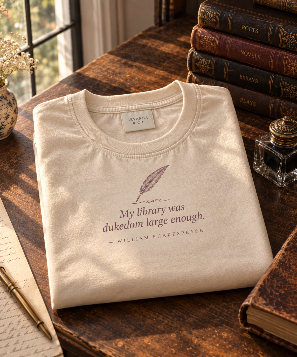 Buttermilk relaxed-fit tee printed with “My library was dukedom large enough.” in mauve serif type, folded on a linen backdrop