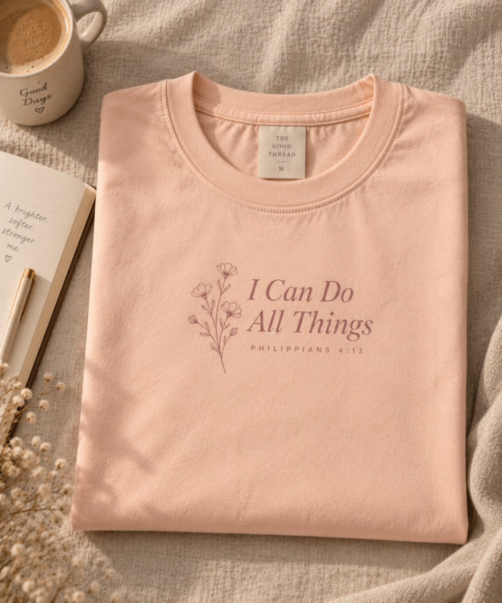Soft Peach relaxed-fit tee printed with “I Can Do All Things” in mauve serif type, folded on a linen backdrop