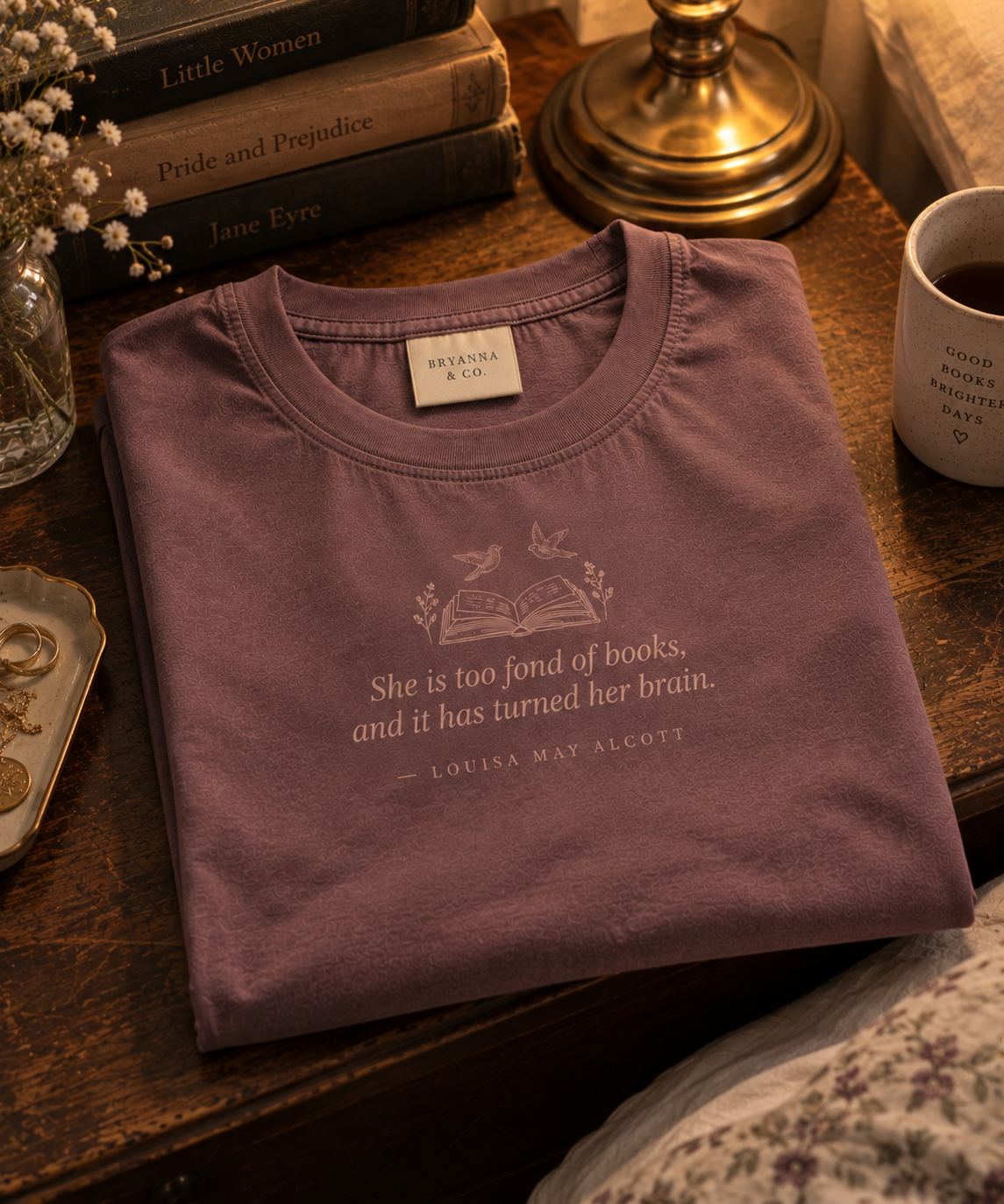 Faded Plum relaxed-fit tee printed with “She is too fond of books, and it has turned her brain.” in mauve serif type, folded on a linen backdrop