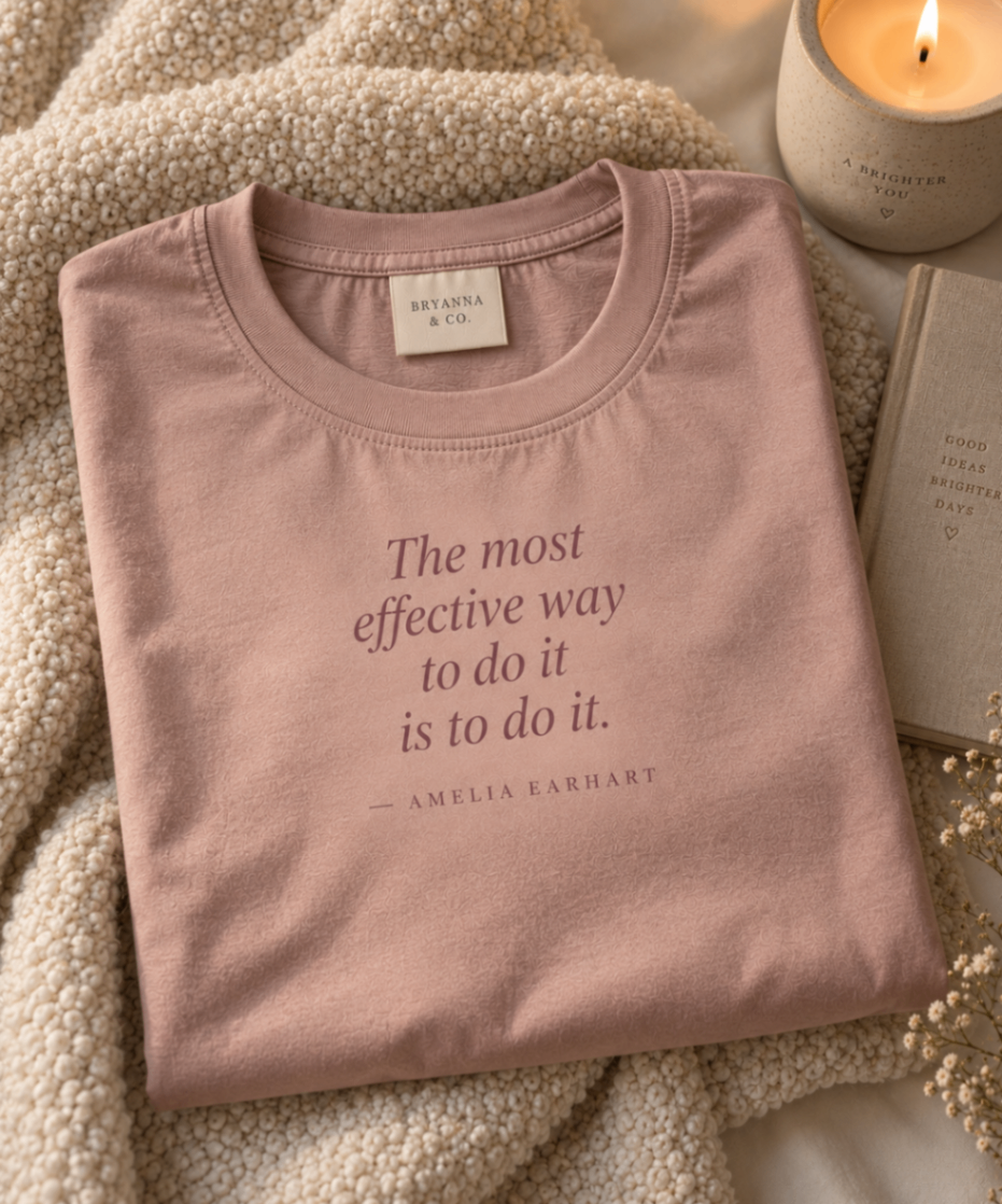 Dusty Mauve relaxed-fit tee printed with “The most effective way to do it is to do it.” in mauve serif type, folded on a linen backdrop